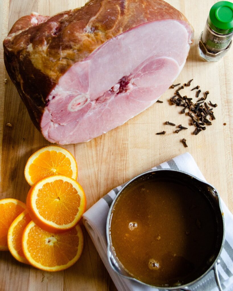 Ham, oranges, cloves and a saucepan of glaze - all ingredients for baked ham.