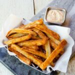 Air Fried Cajun Fries in a paper fry dish with creole dipping sauce behind.