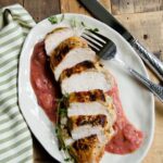Chicken with Orange Rhubarb Sauce on a white oval plate with knife and fork on a wooden table.