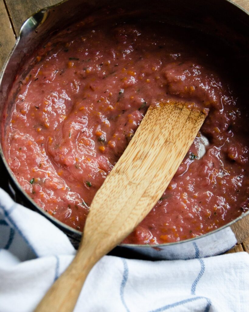 Orange Rhubarb sauce in a saute pan with a wooden spoon.