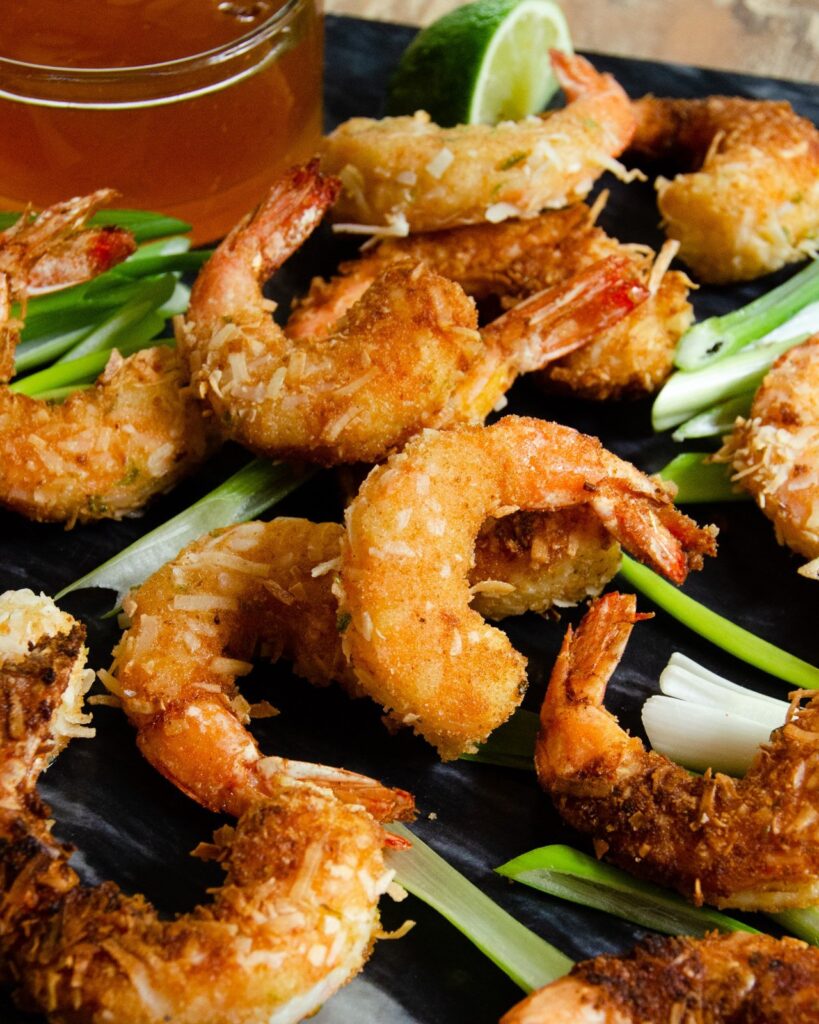 Coconut shrimp on black marble with duck sauce, scallions and lime wedges.