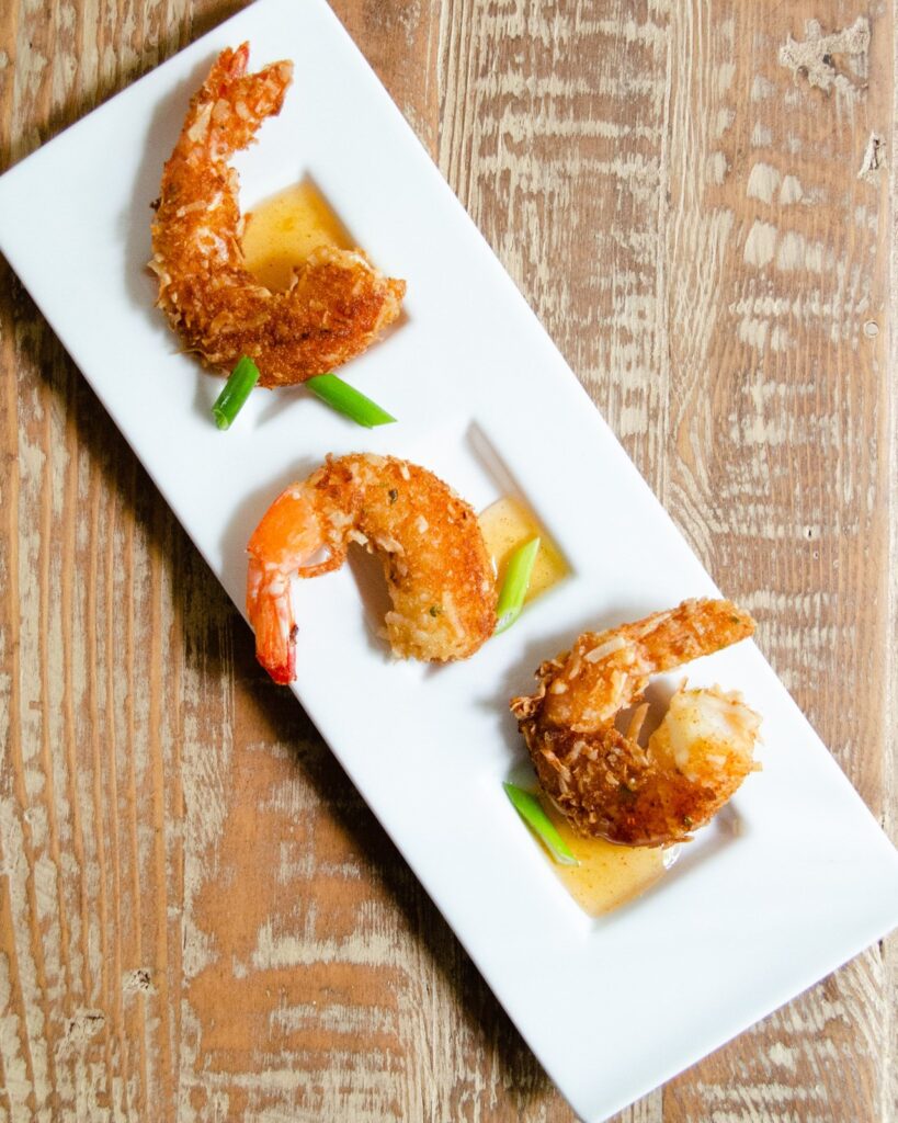 Three coconut shrimp on a white plate with duck sauce.