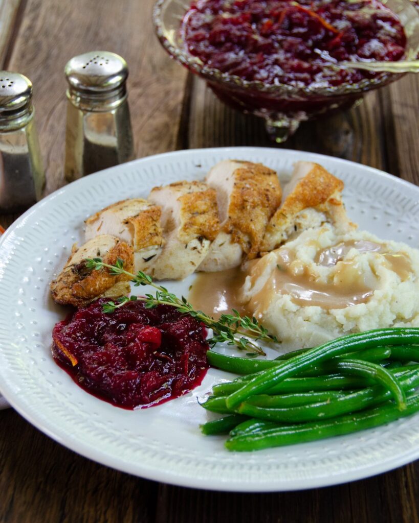 Cranberry Sauce on a white plate with mashed potatoes, chicken and green beans.