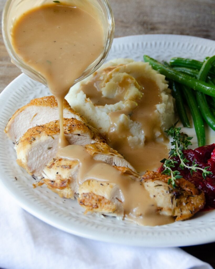 Gravy pouring on sliced chicken with mashed potatoes and green beans.