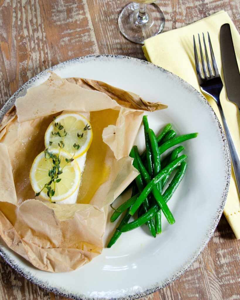 Halibut en papillote on a dinner plate with green beans.