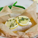Halibut en Papillote on a white plate with green beans.