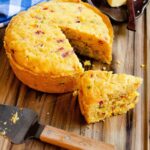 Instant Cornbread on a wooden cutting board with a wedge cut out and butter on the side.