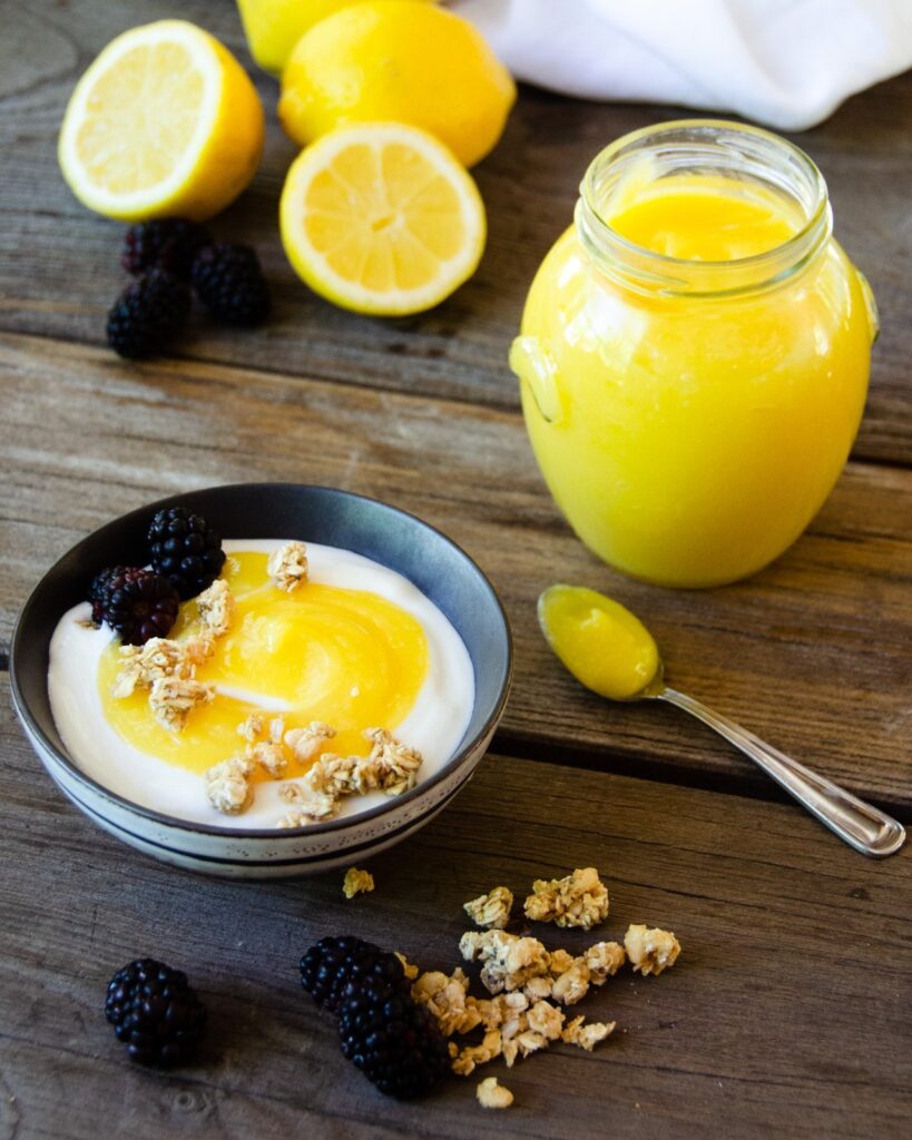 Lemon curd with yogurt and granola in a small bowl with a jar of lemon curd beside it.