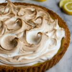 Lemon Meringue Tart on a marble surface with slices of lemons around.
