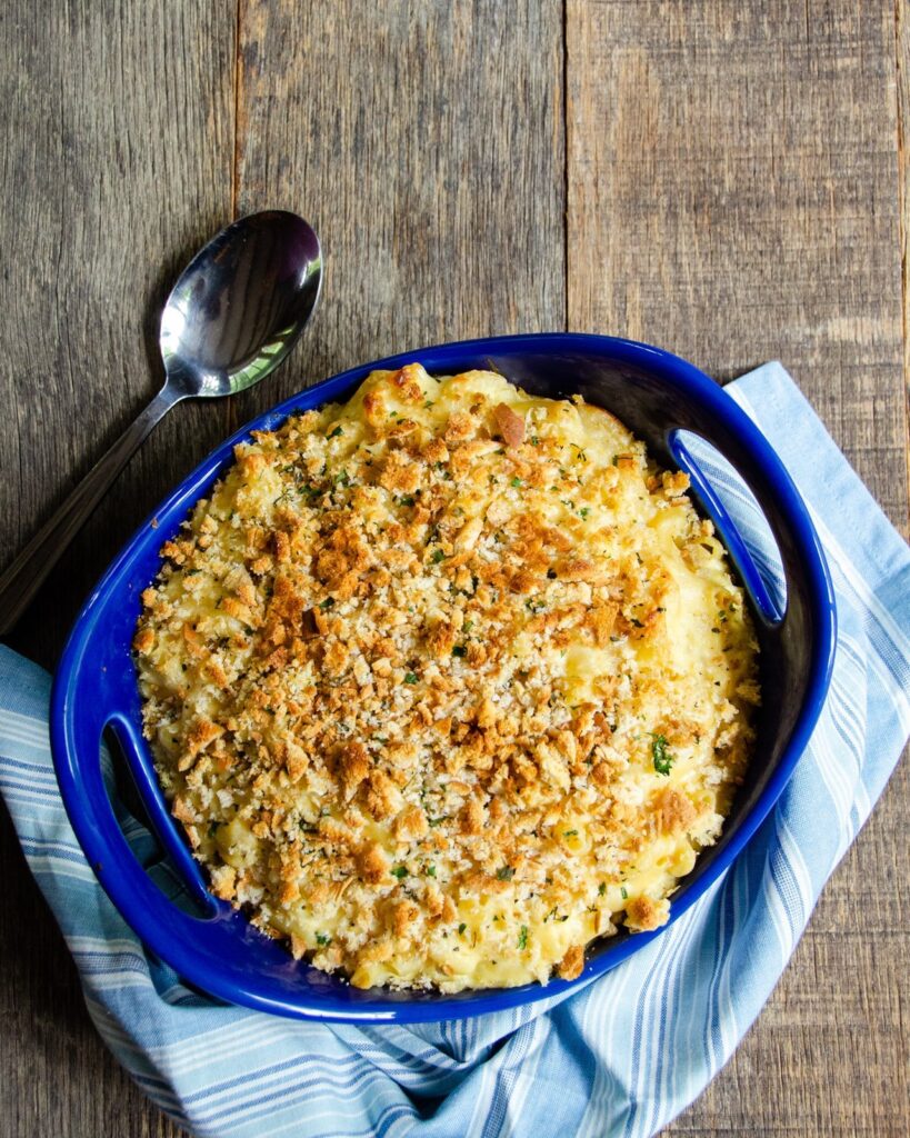 Baked mac and cheese in a blue casserole with spoon and blue towel.