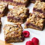 Raspberry Almond Fruit Squares on parchment paper on a wooden cutting board with raspberries scattered around.