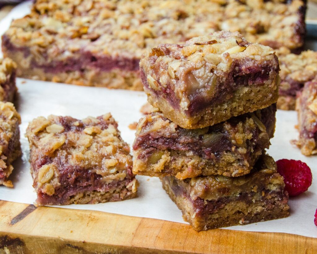 A stack of three raspberry almond fruit squares on parchment paper on a cutting board with more squares around.