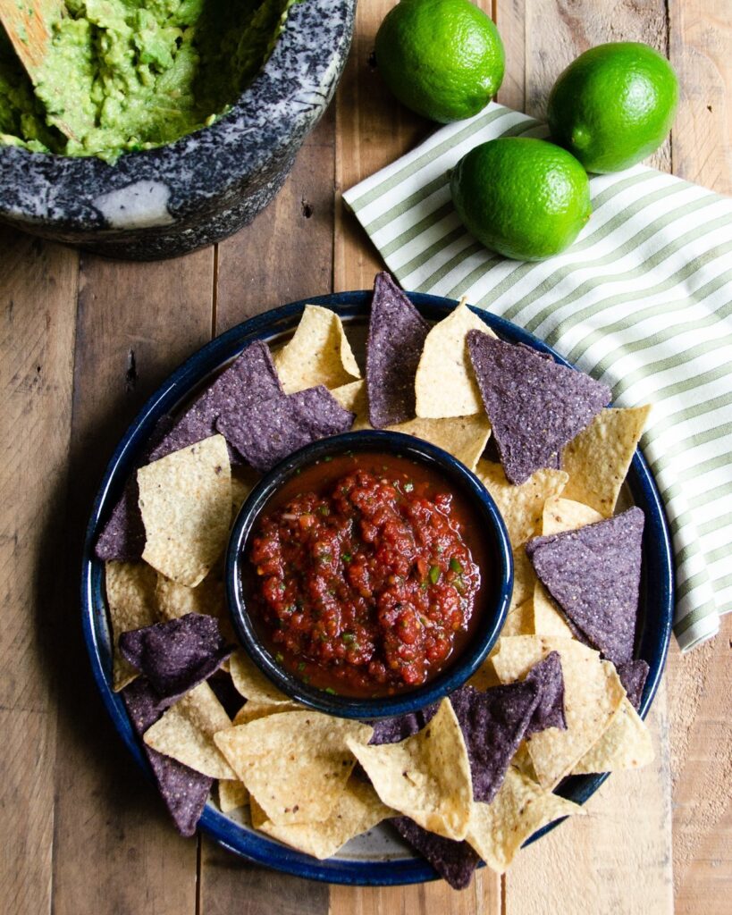 Smooth tomato salsa in a small blue dish with blue and yellow tortilla chips around the outside