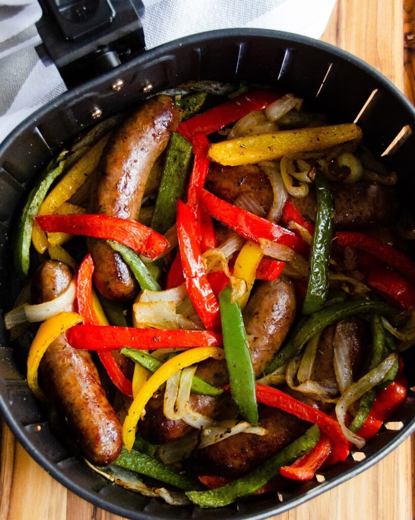 Sausages, onions and peppers in an air fryer basket.
