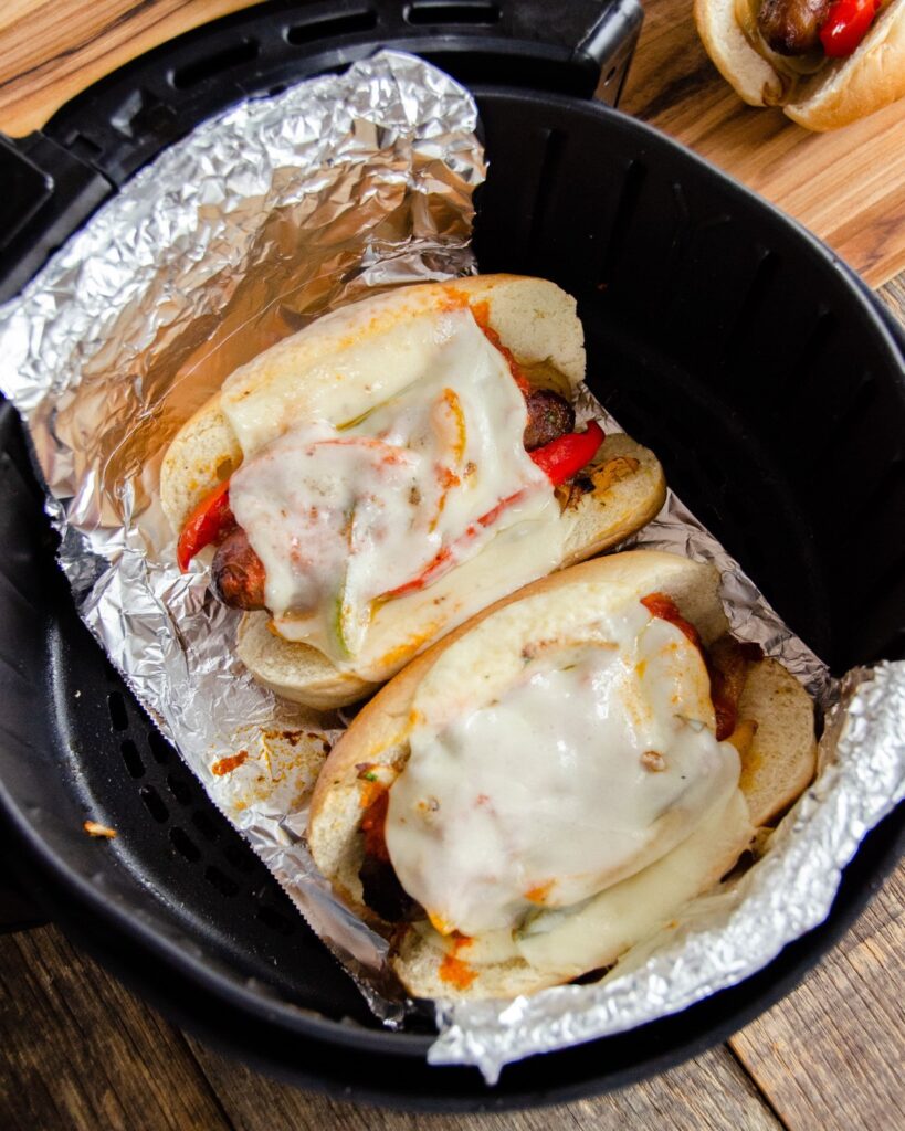 Two sausage sandwiches on an aluminum foil sling in an air fryer basket.
