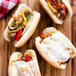 Sausage Sandwiches on a wooden cutting board with a red checkered napkin.