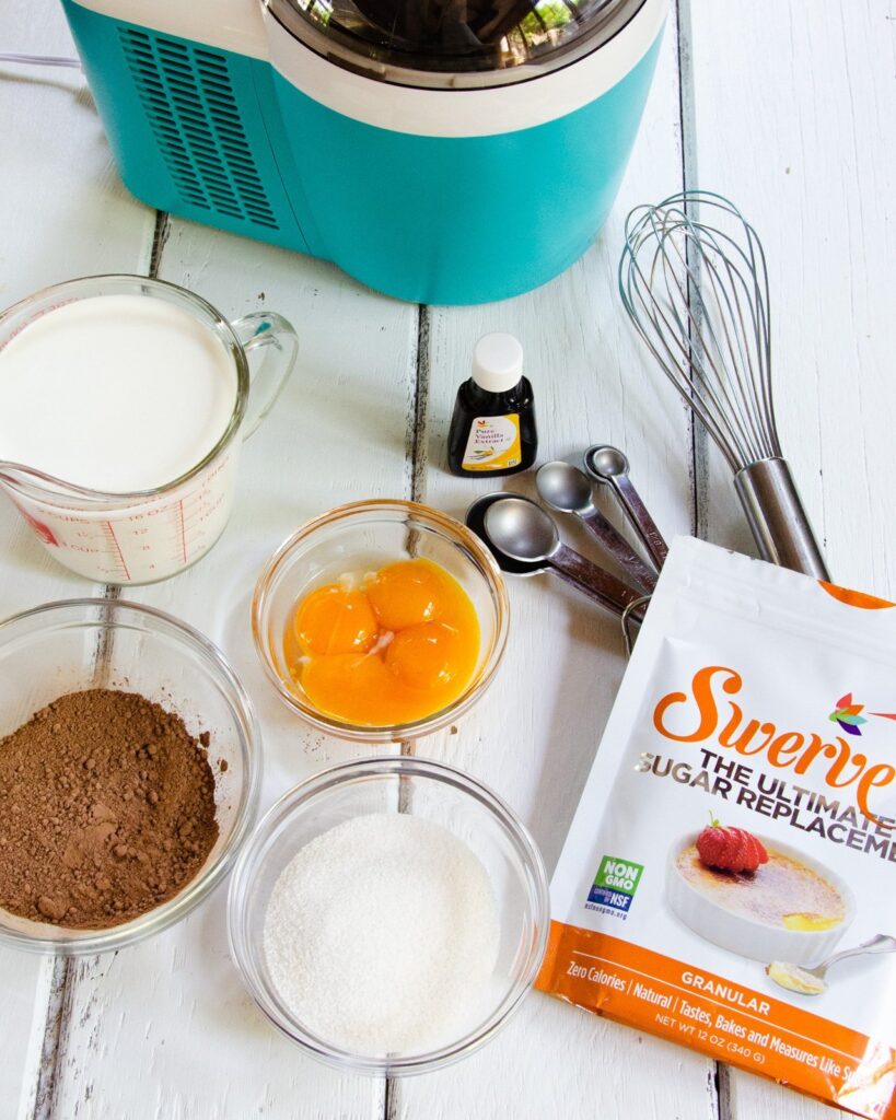 Ingredients for sugar free chocolate ice cream and an ice cream maker on a white wooden table.