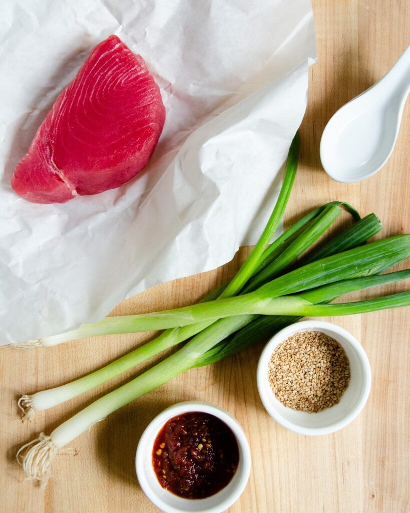 Ahi Tuna on butcher paper with chili garlic sauce, sesame seeds and scallions on a board.