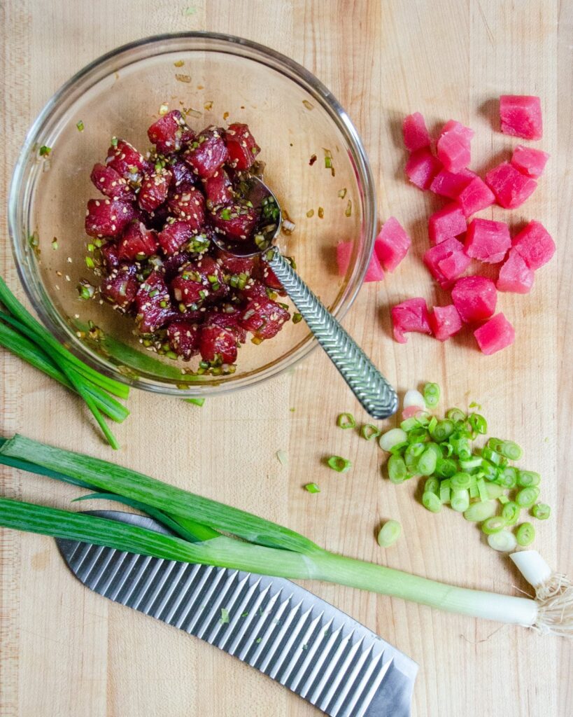 Ingredients for tuna poke - tuna, scallions on a cutting board and mixed tuna poke in a glass bowl.