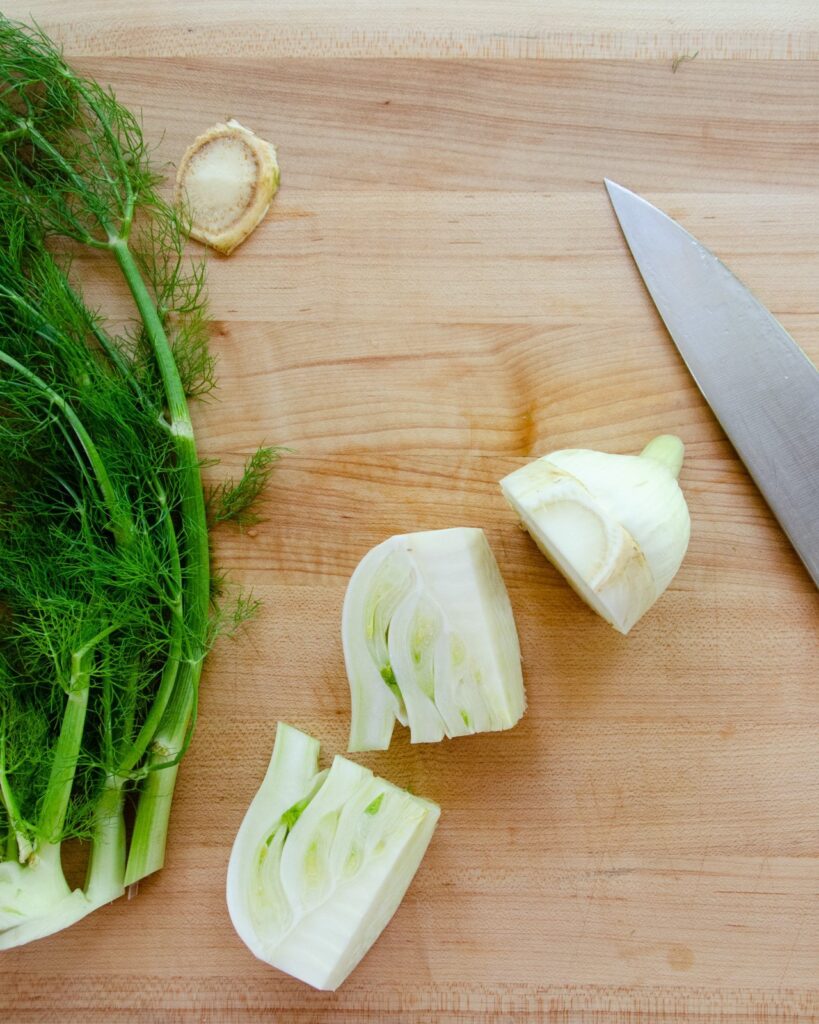 Showing how to cut fennel - stalks and fronds to one side, the bulb cut into a half and two quarters.