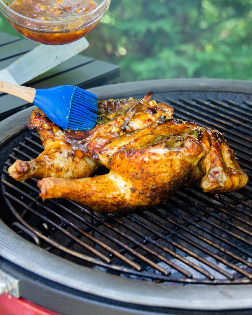 Spatchcocked chicken being basted with glaze on a grill.