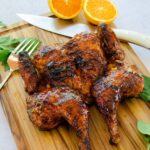 Grilled Spatchcocked Chicken on a cutting board with herbs and halved oranges.