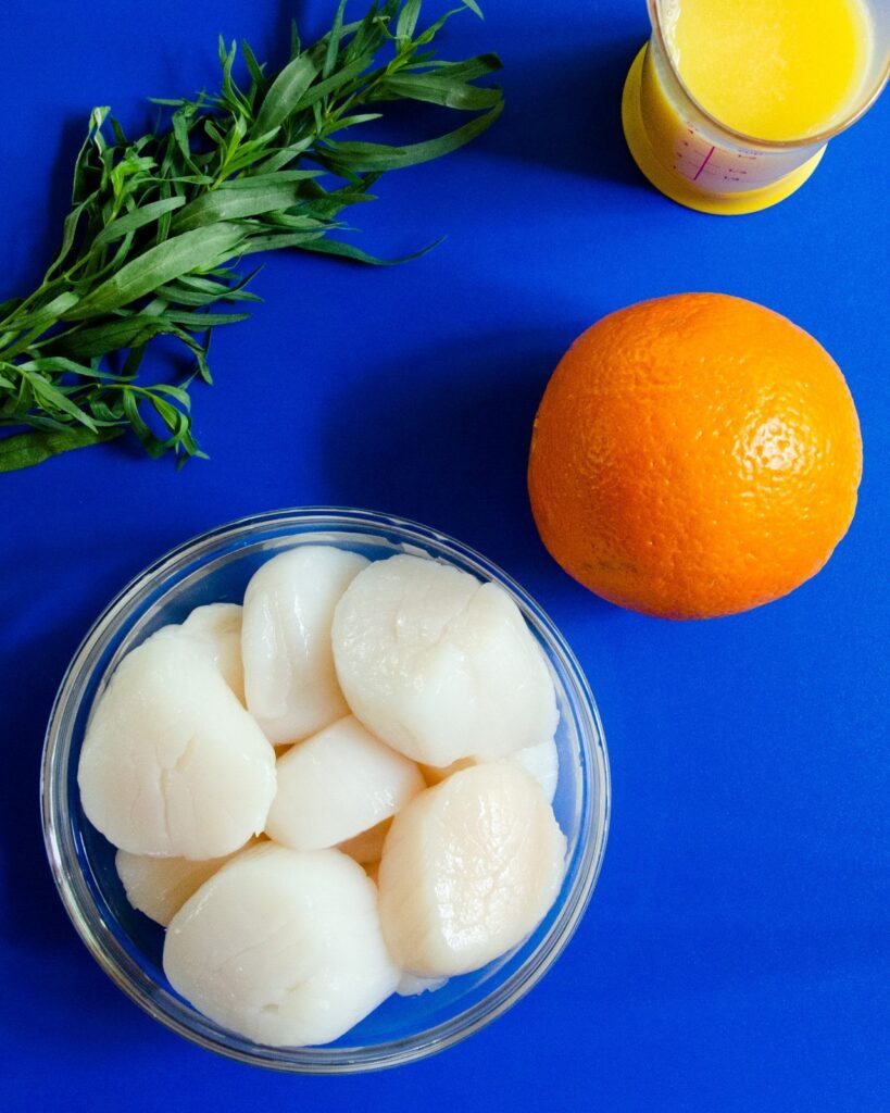 Scallops, tarragon, orange juice and an orange on a blue background.