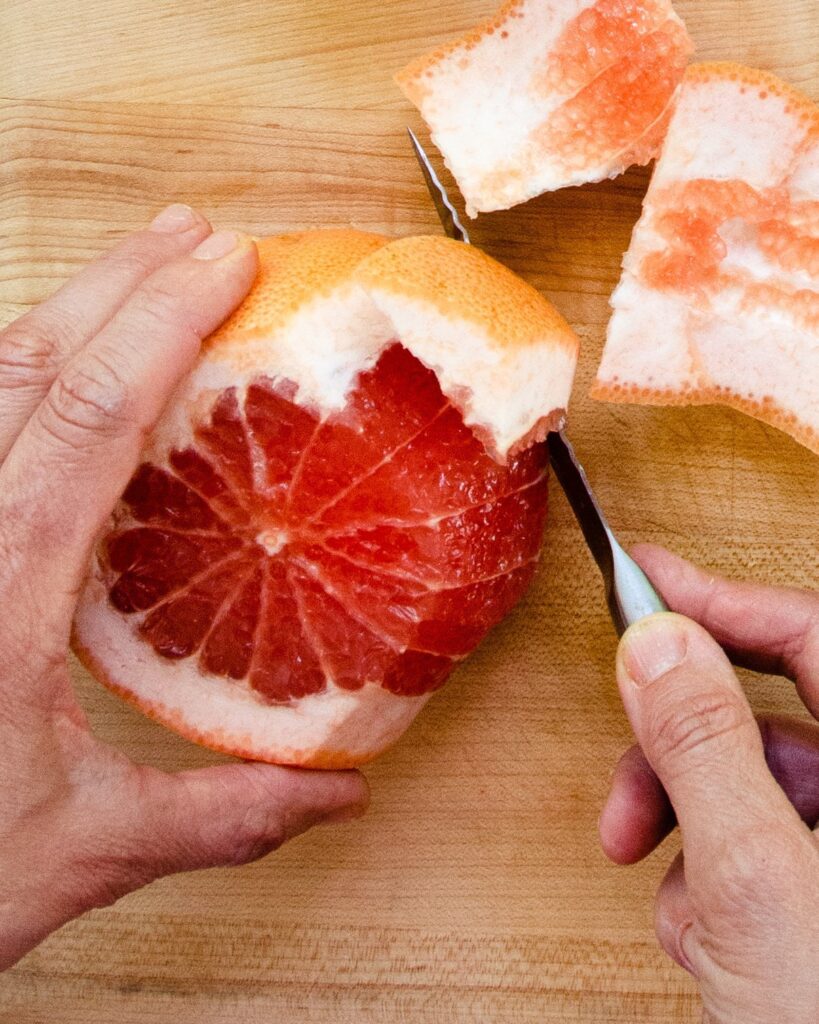 Slicing the peel off a grapefruit as you get ready to supreme citrus fruit.