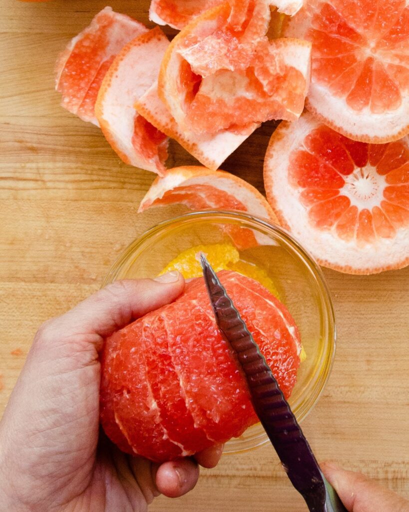 Paring knife slicing down one side of a segment of grapefruit.