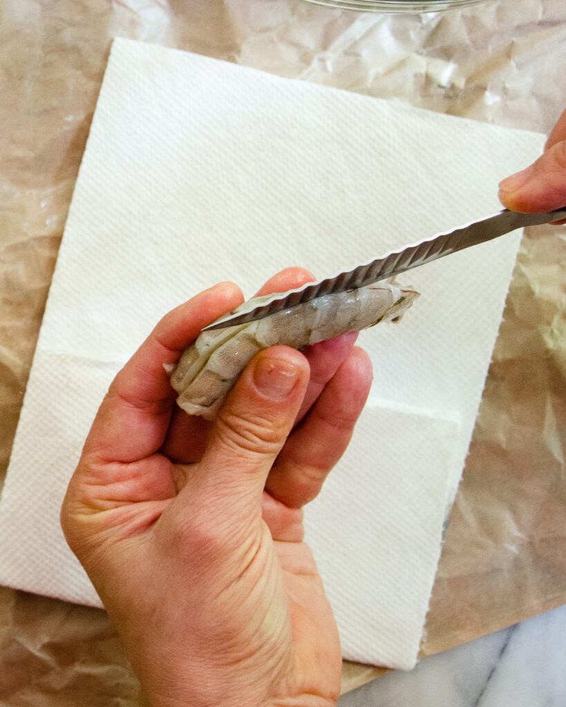 A knife slicing into the back of a shrimp - the first step in deveining a shrimp.