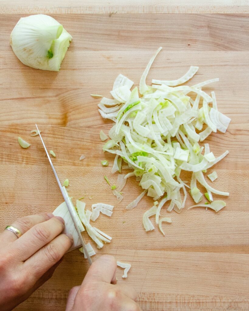 Fennel being sliced on a wooden cutting board.