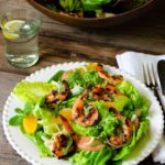 Grilled shrimp and citrus salad on a white plate on a wooden table with salad bowl in background.