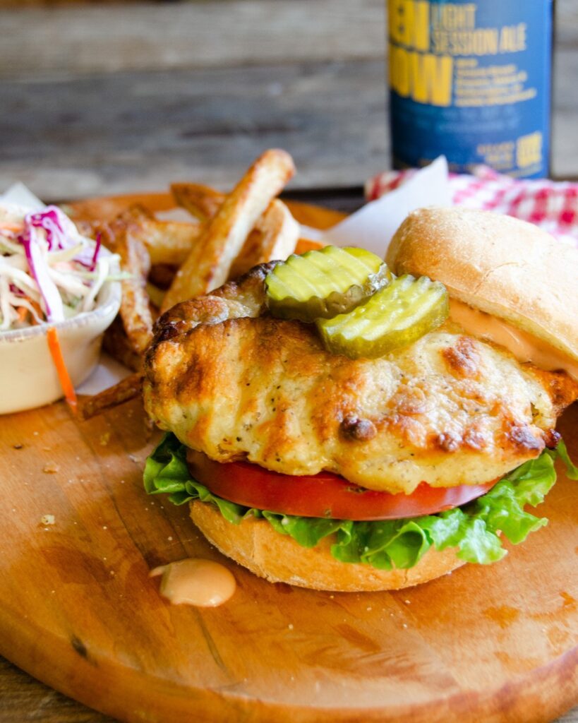 Assembling an air-fried chicken sandwich with a bottle of beer in the background.