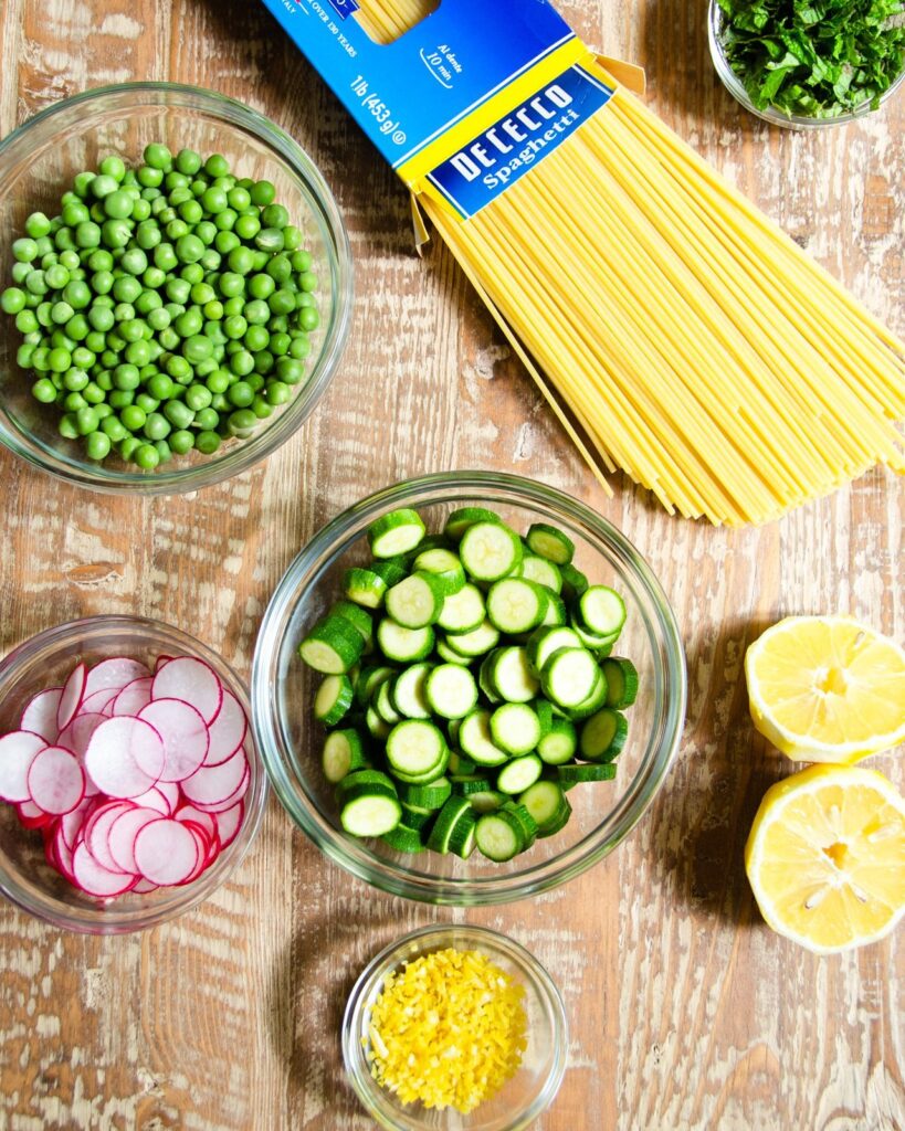 Ingredients for Spaghetti with Zucchini, Peas, Radishes and Mint on a wooden table.