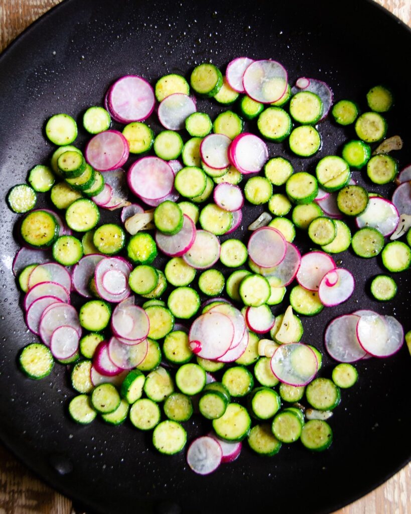 Radishes and baby zucchini cooking in a skillet.