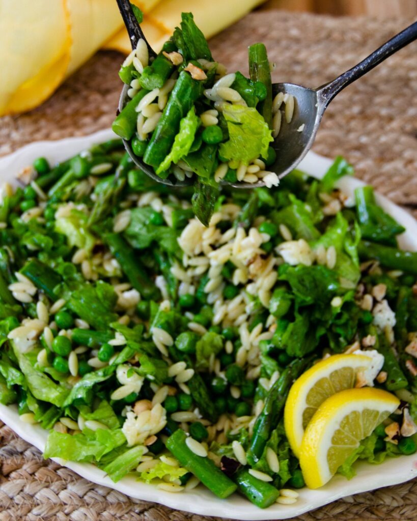 Salad servers living some spring green salad from an oval platter.