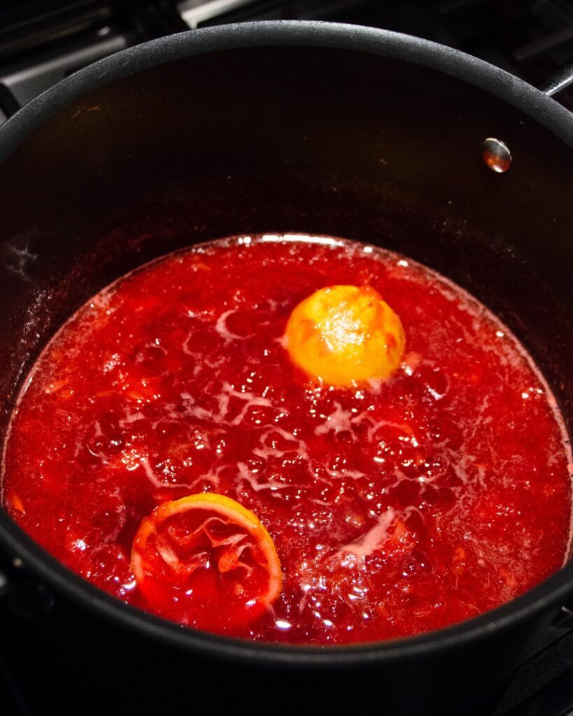 Strawberry  Rhubarb Jam simmering in a pot with lemon halves.
