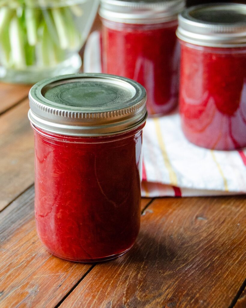 Three jars of strawberry rhubarb jam on a wooden table.