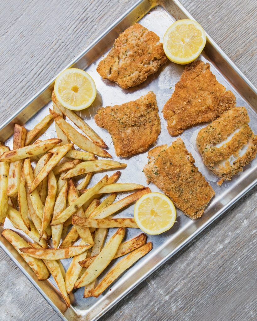 Sheet pan fish and chips on a baking sheet with lemon halves.