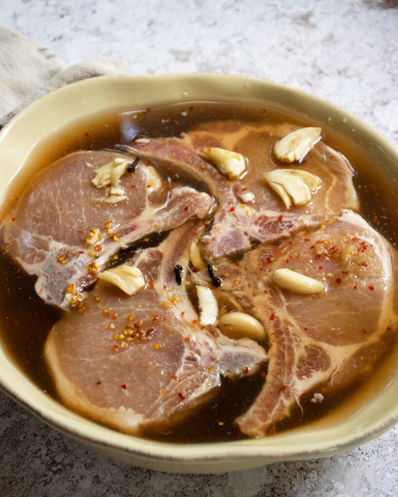 Pork chops sitting in a shallow dish of brine.