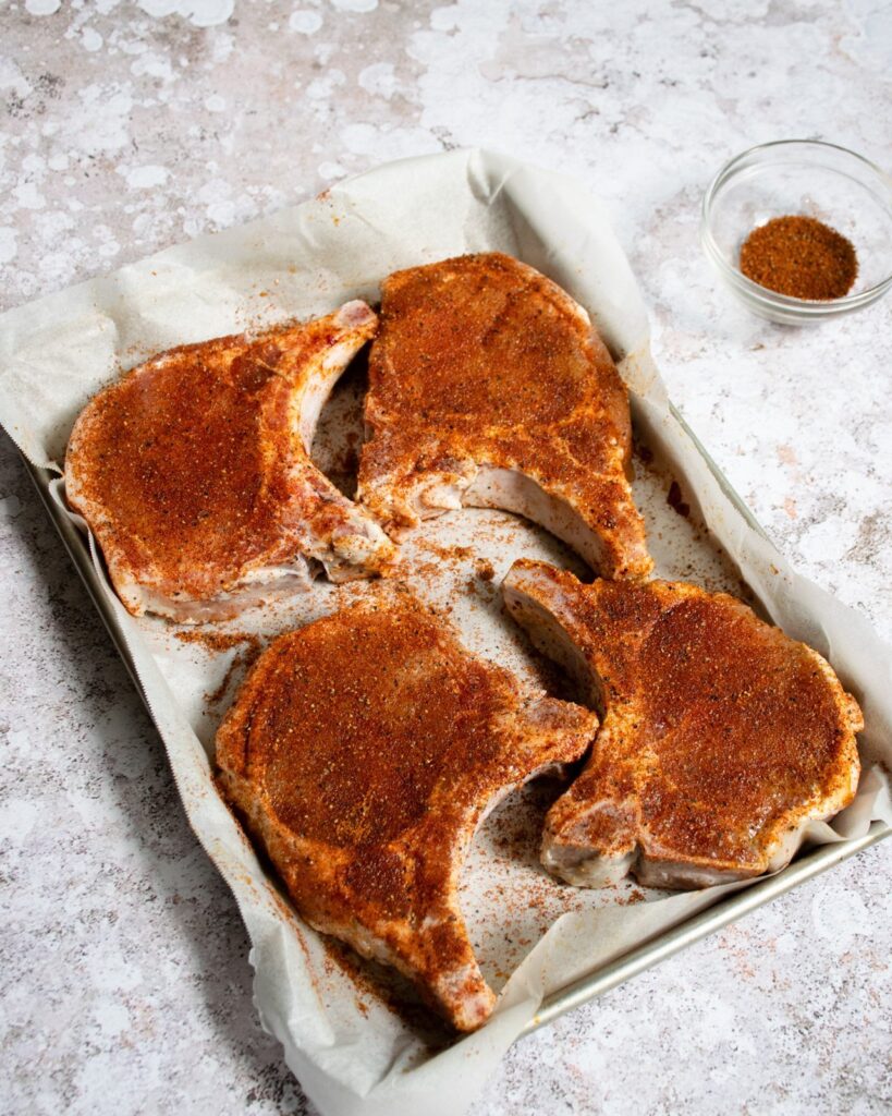 Pork chops on a parchment-lined quarter sheet pan with a spice rub.
