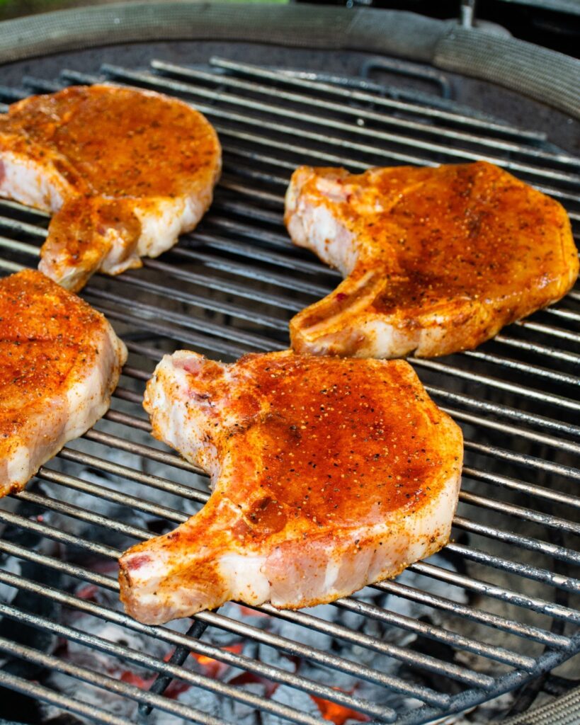 Spice rubbed pork chops on a charcoal grill grate.