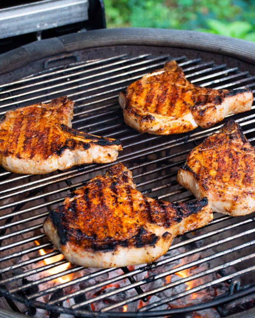Pork chops cooking on a charcoal grill.