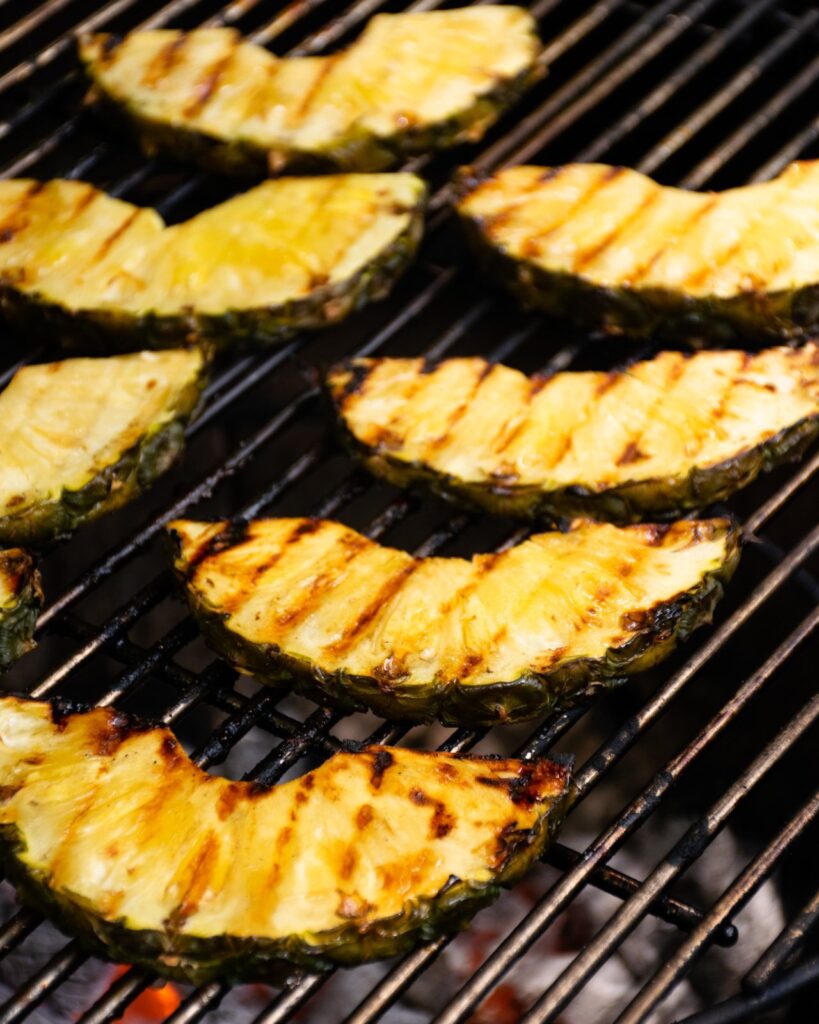 Pineapple slices on a charcoal grill grate.