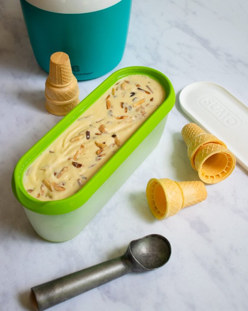 Brown Butter ice cream in a long green container with scoop and sugar cones near by.