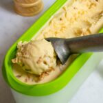 A scoop of brown butter rum ice cream being taken out of the container with a sugar cone nearby.