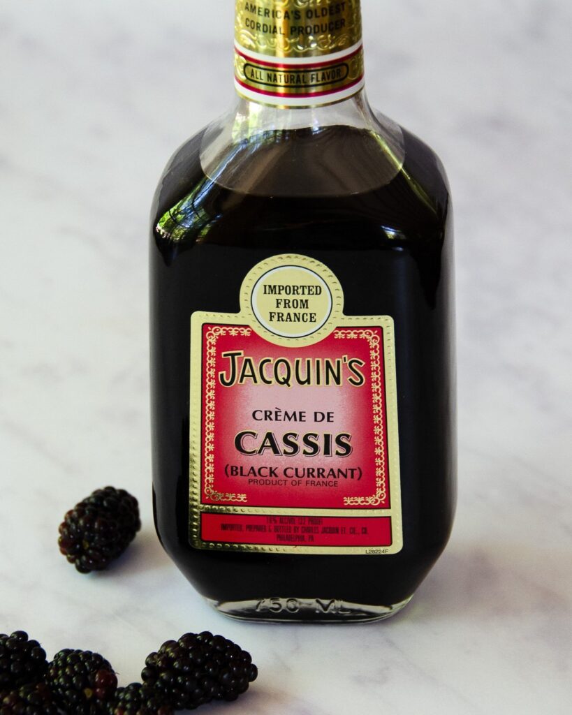 Aa bottle of cassis liquor with blackberries next to it on a marble counter.