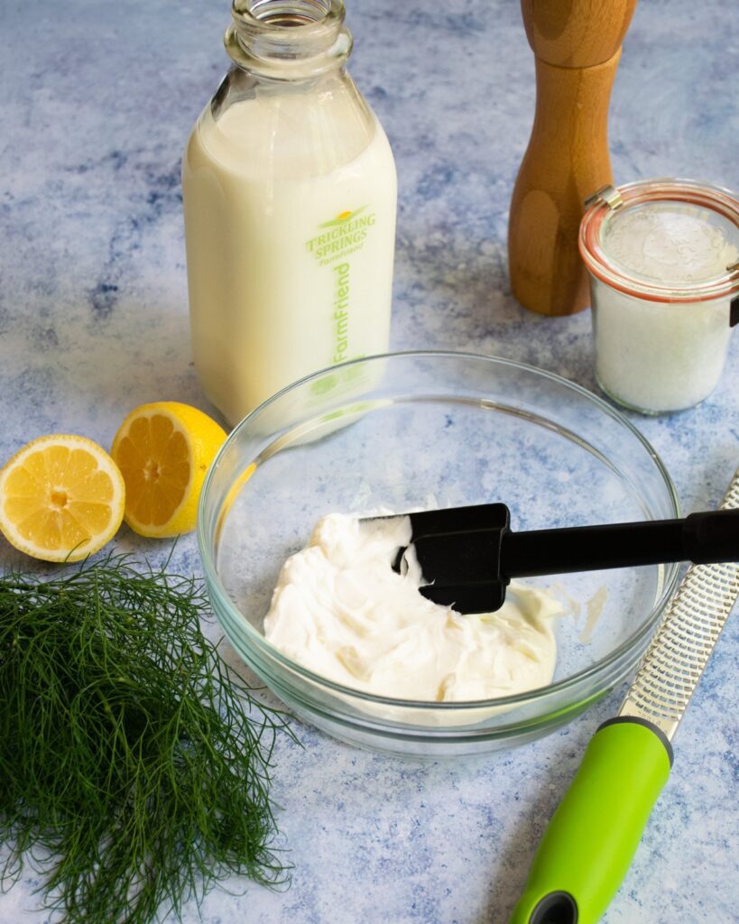 Ingredients for Lemon Dill Buttermilk Dressing with a zester and spatula on a blue marble surface.