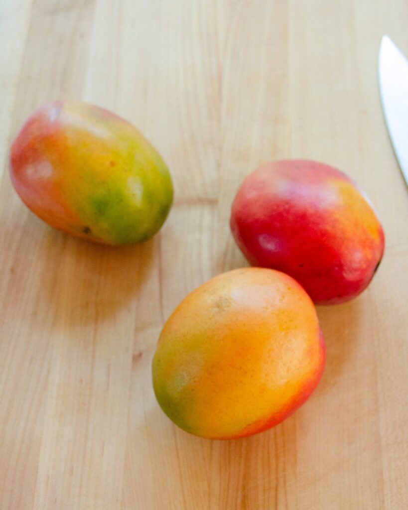 Three mangoes on a cutting board.