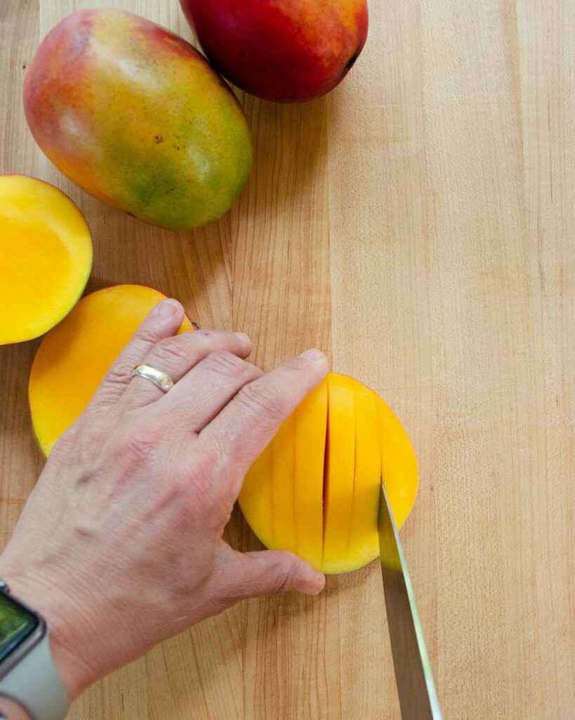 A knife cutting slices into half a mango.
